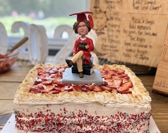 Könnte beinhalten: Ein mehrstöckiger Kuchen, der mit Erdbeeren und roten Streuseln verziert ist. Eine kleine Figur eines Absolventen mit roter Mütze und Robe sitzt oben auf dem Kuchen.