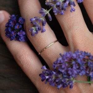 K&ouml;nnte beinhalten: Ein zarter goldener Ring mit geh&auml;mmerter Textur, getragen an einem Finger, der mit violetten Lavendelbl&uuml;ten geschm&uuml;ckt ist.