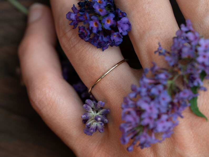 K&ouml;nnte beinhalten: Ein zarter Goldring, getragen an einem Finger, der mit violetten Blumen geschm&uuml;ckt ist.