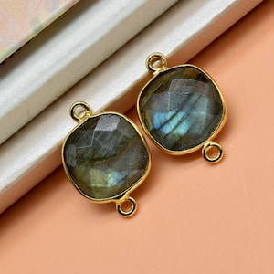 May include: Two gold-toned gemstone connectors with a square shape and a dark blue labradorite stone. The connectors have two jump rings on each side.