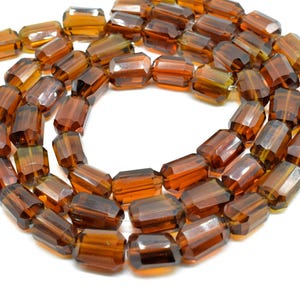 Puede incluir: Un collar de cuentas facetadas de color ámbar. Las cuentas son rectangulares con bordes cortados, creando un efecto brillante. Las cuentas están ensartadas, formando un collar o una pulsera.