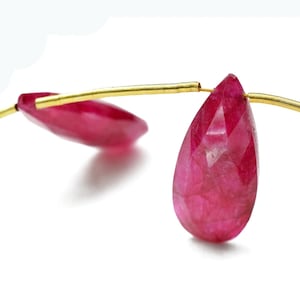 Op de afbeelding: Twee facetgeslepen robijn edelsteen kralen geregen aan een gouden draad met een rode kwast aan het einde.