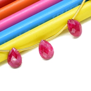 May include: A strand of gold beads with four teardrop-shaped ruby red gemstone beads hanging from it.