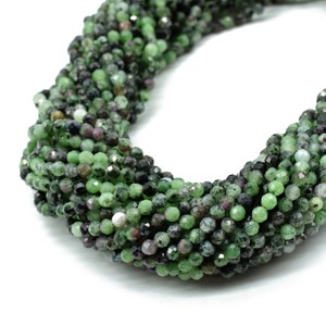 May include: A strand of green, black, and pink gemstone beads. The beads are round and have a faceted finish.