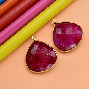 Peut inclure: Deux pendentifs en forme de larme avec des montures dorées et une pierre précieuse rose foncé. Les pierres précieuses ont une taille facetée.