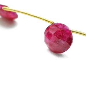 May include: Two red gemstone beads strung on a gold wire. The beads are faceted and have a round shape.