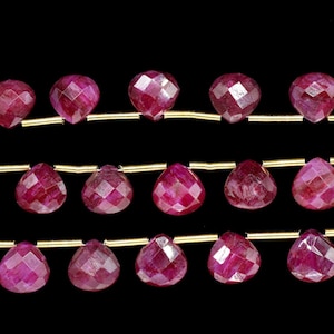 Pode incluir: Um fio de contas de rubi, cada conta é facetada e tem a forma de uma lágrima. As contas são enfiadas em um fio de ouro.