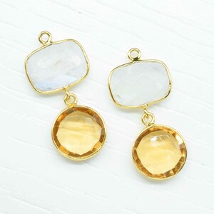Peut inclure: Une paire de boucles d'oreilles en or avec deux pierres chacune. La pierre du haut est une pierre de lune rectangulaire blanche. La pierre du bas est une citrine ronde jaune.