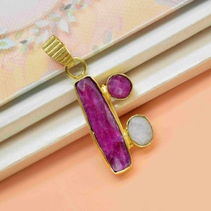 May include: A gold pendant with a pink rectangular gemstone and two smaller round gemstones, one pink and one white.