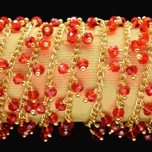 May include: A gold chain with red glass beads hanging from it. The chain and beads are arranged in a layered pattern.
