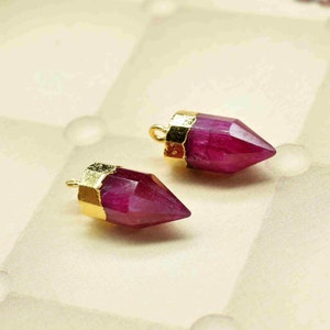 Może przedstawiać: Dwa złote, spiczaste, różowe zawieszki z kamieni szlachetnych. Kamienie szlachetne są fasetowane i mają przezroczysty wygląd.