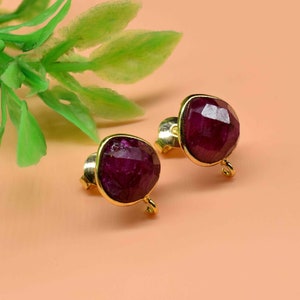 Pode incluir: Um par de brincos de ouro com uma pedra preciosa de cor roxa escura. Os brincos têm um design simples e são perfeitos para o uso diário.