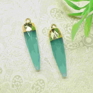 Puede incluir: Dos colgantes de piedra preciosa azul turquesa con tapas doradas. Los colgantes tienen forma de lágrimas largas y delgadas.