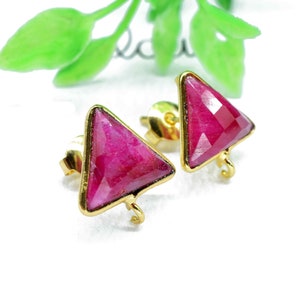 Może przedstawiać: Para złotych kolczyków z trójkątnymi różowymi kamieniami szlachetnymi. Kolczyki mają prosty design i są idealne do codziennego noszenia.