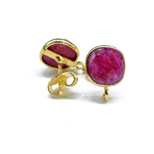 Könnte beinhalten: Ein Paar goldene Ohrringe mit roten Edelstein-Akzenten. Die Ohrringe haben einen Steckerverschluss.