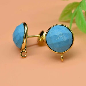 May include: A pair of gold earrings with blue gemstone accents. The gemstones are round and have a faceted design. The earrings have a simple post back.