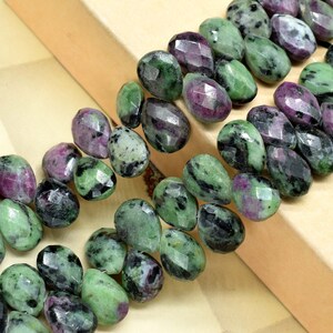 May include: A strand of green, black, and pink gemstone beads. The beads are faceted and have a teardrop shape.