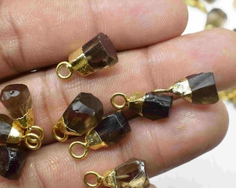 Puede incluir: Una colección de colgantes de piedras preciosas marrones con anillas de salto doradas. Las piedras preciosas tienen una forma irregular y un aspecto natural y en bruto.