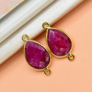 Puede incluir: Dos colgantes de forma de lágrima de color dorado con incrustaciones de piedras preciosas rosas. Cada colgante tiene un bucle a cada lado para sujetarlo a una cadena o cordón.