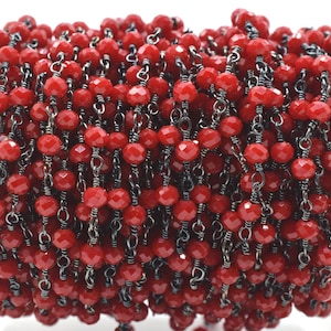 Peut inclure: Gros plan d'une chaîne de perles de cristal rouge avec des maillons de chaîne en métal noir. La chaîne est enroulée en spirale.