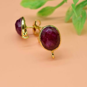 May include: A pair of gold earrings with a deep red gemstone. The earrings have a simple design and are perfect for everyday wear.