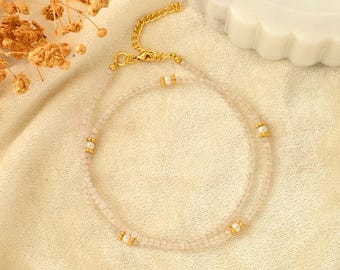 Könnte beinhalten: Eine zarte Halskette mit zwei Reihen kleiner rosa Perlen und goldenen Akzenten. Die Halskette ist mit kleinen weißen Perlen verziert, die gleichmäßig verteilt sind.