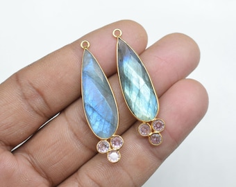 May include: Two gold-plated teardrop-shaped pendants with a blue labradorite stone and three pink stones at the bottom.