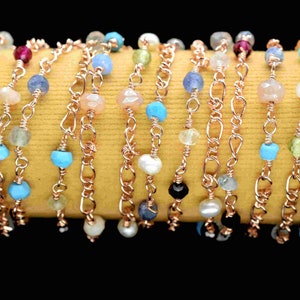 May include: A close-up of a multi-strand necklace with a variety of gemstone beads and rose gold chain links. The beads are in shades of blue, turquoise, pink, green, white, and black.