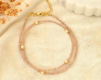 Könnte beinhalten: Eine zarte Halskette mit zwei Reihen rosa Perlen und goldenen Akzenten. Die Halskette ist mit kleinen weißen Perlen verziert, die zwischen den Perlen verteilt sind.
