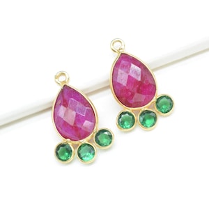 May include: A pair of gold-tone earring charms featuring a pink teardrop-shaped gemstone with three smaller green round gemstones.