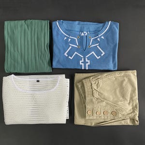 Pu&ograve; includere: Un assortimento di capi di abbigliamento piegati su una superficie scura. Include un top verde plissettato, una camicia azzurra con un disegno geometrico bianco, un top in rete bianco e pantaloni color cachi con bottoni.
