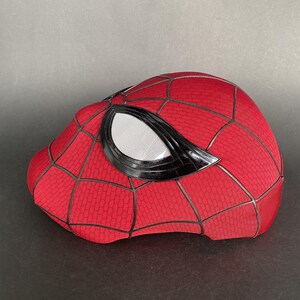 May include: A red Spider-Man mask with a textured pattern and black webbing. The mask features large white eye lenses with a black border. The overall design is a replica of the superhero's iconic head covering.