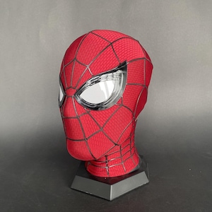 May include: A red and black Spider-Man mask with silver-framed eye lenses. The mask features a web pattern and is displayed on a black stand. The mask is made of a textured material.