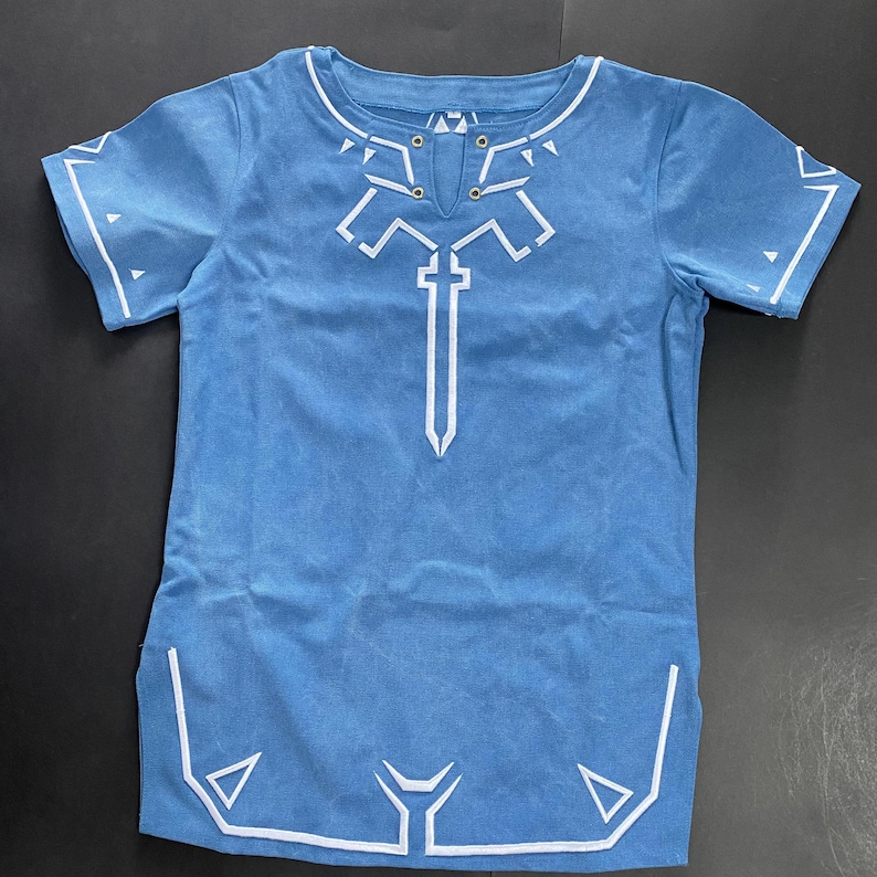 Pu&ograve; includere: Una maglietta azzurra con un design geometrico bianco. Il design include una spada e altre forme. La maglietta ha un girocollo e maniche corte. Il tessuto &egrave; morbido.