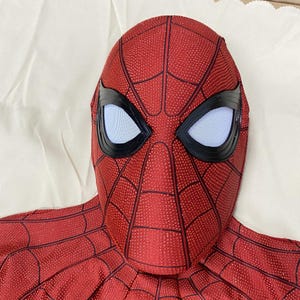 May include: A red and black Spider-Man mask with white eye lenses and a webbed pattern. The mask is made of a textured material and is designed to cover the entire head. The eye lenses are outlined in black.