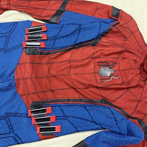 May include: Red and blue Spider-Man costume with a web pattern. The costume features a black spider emblem on the chest and black accents. The blue sections have a textured pattern, and the costume has several red and black clasps.