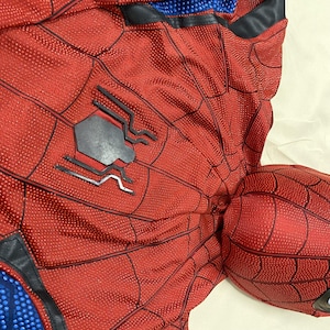 May include: Red and black Spider-Man costume with a web pattern. The costume features a black spider emblem on the chest and blue accents. The fabric has a textured appearance.