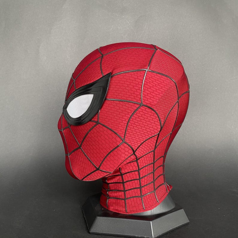 May include: A red and black Spider-Man mask, featuring a textured pattern and black web detailing. The mask has white mesh eye coverings and is displayed on a black stand. The mask is a cosplay item.