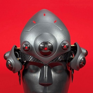 May include: A gray helmet with multiple red glowing eyes. The helmet is worn on a mannequin head.