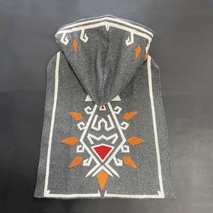 May include: Grey hooded cape with white and orange geometric patterns. The cape has a hood and a decorative design on the back, with a red diamond shape at the centre of the design. The edges are trimmed with white.