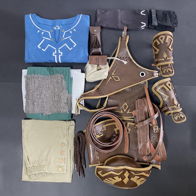 Pu&ograve; includere: Una collezione di costumi cosplay, tra cui una camicia blu con disegni geometrici bianchi, un'armatura in pelle marrone, pantaloni kaki e cotta di maglia. L'ensemble comprende anche guanti, tasche e una cintura.