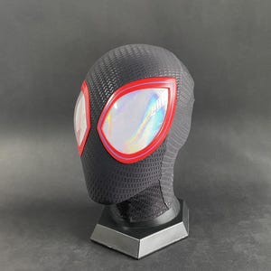 May include: Black and red Spider-Man mask with iridescent lenses. The mask is on a black stand.