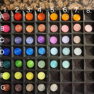 May include: A close-up of a black tray with 8 rows of colourful round chips. The chips are arranged in rows labelled A through H, with numbers 1 through 8 at the top of the tray.