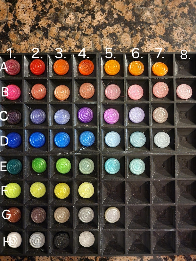 May include: A close-up of a black tray with 8 rows of colourful round chips. The chips are arranged in rows labelled A through H, with numbers 1 through 8 at the top of the tray.