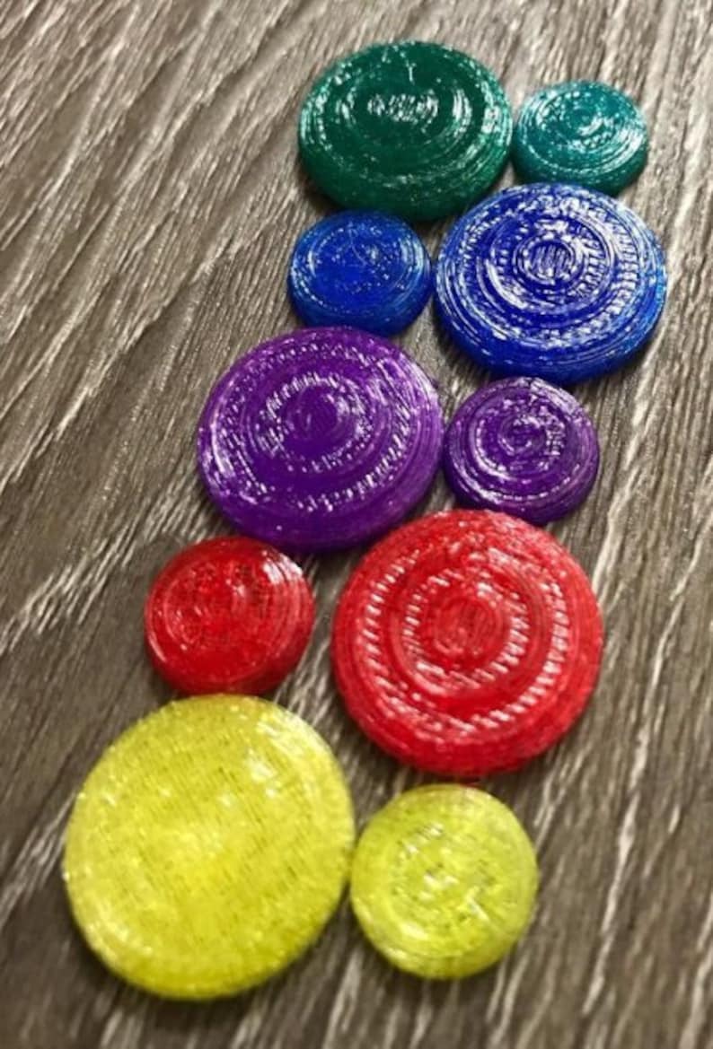 May include: A set of colourful, round, decorative, 3D printed discs with a concentric circle pattern. The discs are arranged in a rainbow pattern, starting with green, blue, purple, red, and yellow.