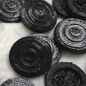 May include: A collection of black, round, decorative buttons with a concentric circle design. The buttons are made of a smooth, shiny material.