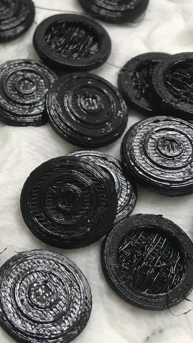May include: A collection of black, round, decorative buttons with a concentric circle design. The buttons are made of a smooth, shiny material.