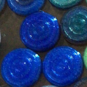 May include: A collection of round, iridescent glass tiles in shades of blue, green, and white. The tiles have a textured surface and a slightly raised centre.