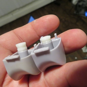 Op de afbeelding: Twee grijze plastic knoppen met witte plastic stelen. De knoppen hebben een afgeronde vorm en zijn ontworpen voor een videogamecontroller.