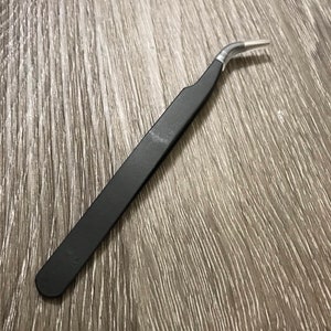 May include: Black angled tweezers with a silver tip.